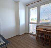 Kuchyně v 1-pokojovém bytě s podlahou s dřevěným dekorem, dřezem, stolem a židlemi.