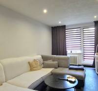 Obývací pokoj v dvoupokojovém bytě s pohovkou, konferenčním stolkem a dětskou postýlkou.