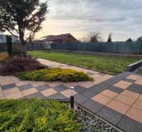 Zahrada u rodinného domu na Větrné ulici v Krakovanech s dlažbou a terasou.