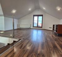 Podkrovní místnost s podlahou s dřevěným dekorem, schodištěm a velkým oknem.