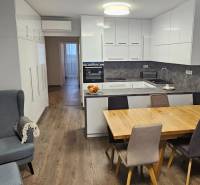 Kuchyně v 3pokojovém bytě s podlahou s dřevěným dekorem, jídelním stolem a světlým nábytkem.