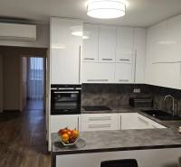 Kuchyně s bílými skříňkami, tmavou pracovní deskou a podlahou s dřevěným dekorem ve 3pokojovém bytě.