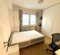 Ložnice ve 4pokojovém bytě s postelí, skříní a podlahou s dřevěným dekorem.