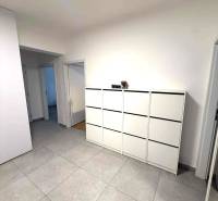 Prostorná chodba se světlými dlaždicemi a bílou komodou ve 4pokojovém bytě.