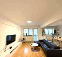 Obývací pokoj ve 4pokojovém bytě s podlahou s dřevěným dekorem a černou sedačkou.