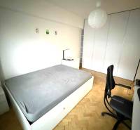 Ložnice s vestavěnými skříněmi, podlahou s dřevěným dekorem a jednoduchým nábytkem ve 4pokojovém bytě.