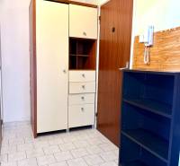 Chodba 1-pokojového bytu s dlažbou, skříňkami a telefonem na stěně.