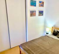 Ložnice v dvoupokojovém bytě s postelí, vestavěnou skříní a dekoracemi na stěně.