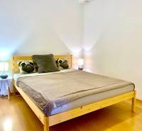 Ložnice v dvoupokojovém bytě s dřevěným dekorem a polštáři na posteli.