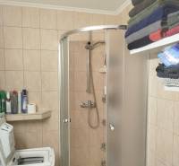 Koupelna v garsonce s pračkou, sprchovým koutem, regálem a uloženými ručníky.