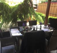 Rodinný dům s posezením na terase, včetně podlahy s dřevěným dekorem a zahradní zeleně.