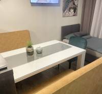 Obývací část s TV v rodinném domě, skleněný stůl, pohovky, obraz páva, podlaha s dřevěným dekorem.