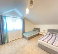 Podkrovní pokoj se dvěma postelemi a jemným kobercem v rodinném domě.