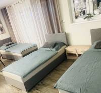 Tři postele, dva noční stolky a podlaha s dřevěným dekorem v rodinném domě.