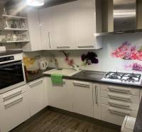 Kuchyně v rodinném domě s bílými skříňkami, dekorativním obkladem a podlahou s dřevěným dekorem.