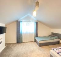 Ložnice v rodinném domě se dvěma postelemi, televizí a kobercovou podlahou.