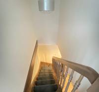 Schodiště s kobercem vede nahoru, nad ním visí svítidlo v rodinném domě.