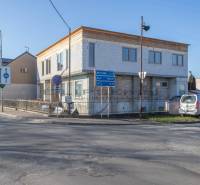 Budova ve Velkých Levárech, u cesty, s zaparkovaným autem a dopravními značkami.