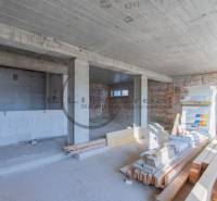 Interiér budovy ve výstavbě s nerovnou cihlovou stěnou a stavebním materiálem na podlaze.