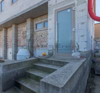 Budova ve Velkých Levárech s nedokončenou fasádou a schody na betonovém základu.