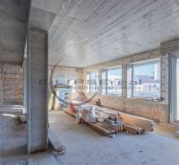 Interiér budovy s cihlovými stěnami, velkými okny a stavebním materiálem.