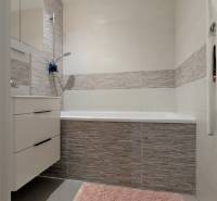 Koupelna s vanou, šedými obklady a růžovým kobercem ve 3-pokojovém bytě.