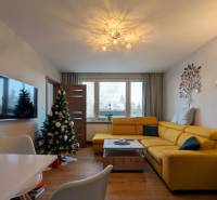 Obývací pokoj v 3-pokojovém bytě se žlutou sedačkou a podlahou s dřevěným dekorem.