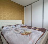 Ložnice v 3-pokojovém bytě s tapetou a vestavěnou skříní, podlaha s dřevěným dekorem.