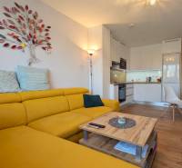 Světlá kuchyně s podlahou s dřevěným dekorem a žlutou sedačkou ve 3-pokojovém bytě.