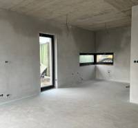 Interiér rodinného domu s betonovými stěnami a velkými okny, vidět neúplnou elektrickou instalaci.