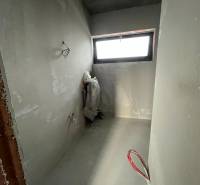 Nedokončená místnost v rodinném domě s oknem a odkrytým potrubím.