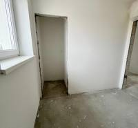 Pokoj v 3-pokojovém bytě s oknem, omítnuté stěny, betonová podlaha, stavební úpravy.