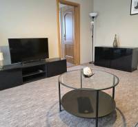 Obývací pokoj ve 3-pokojovém bytě s TV, kulatým stolem a dekorativními prvky.