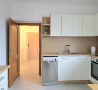 Světlá kuchyně s vestavěnými spotřebiči a podlahou s dřevěným dekorem v 3-pokojovém bytě.