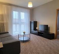 Obývací pokoj v 3-pokojovém bytě s pohovkou, televizí, stolkem a balkónovými dveřmi.