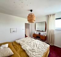 Ložnice v rodinném domě s postelí, zrcadlem a červeným kobercem na podlaze.