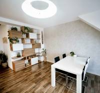 Jídelní stůl, židle a police s dekoračními prvky v 3-pokojovém bytě s podlahou s dřevěným dekorem.