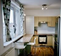 Kuchyně v 3-pokojovém bytě s barovým pultem, podlahou s dřevěným dekorem a velkým oknem.