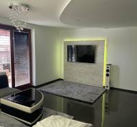 Obývací pokoj v rodinném domě s lesklou podlahou a TV na stěně.