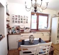 Jídelna v rodinném domě s bílým nábytkem, obrázky na stěně a ozdobným lustrem.