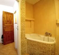 Koupelna v rodinném domě s vanou obloženou kamennými obklady a dřevěnými dveřmi.