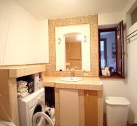 Koupelna rodinného domu s pračkou, umyvadlem a otevřeným oknem.