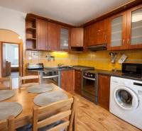 Kuchyně 4pokojového bytu s dřevěným dekorem, vybavená spotřebiči, jídelní stůl, žluté obklady.