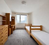 Světlý pokoj s dvěma postelemi, dřevěnými policemi a kobercem ve 4pokojovém bytě.