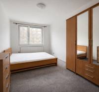 Ložnice ve čtyřpokojovém bytě s dřevěným nábytkem a kobercem.