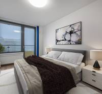 Ložnice v 2-pokojovém bytě s pohodlnou postelí, obrazem a lampou na nočním stolku.