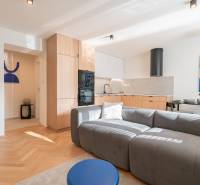 Obývací část 3pokojového bytu s kuchyní, šedou pohovkou a podlahou s dřevěným dekorem.