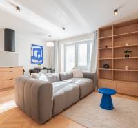 Světlý obývací pokoj v 3-pokojovém bytě s pohovkou, dřevěným dekorem a modrými doplňky.