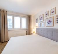 Světlá ložnice s podlahou s dřevěným dekorem, postelí a nástěnnými obrazy v 2pokojovém bytě.