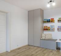 Dětský pokoj s podlahou s dřevěným dekorem, skříňkou na stěně a knihovničkami.